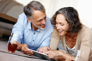 Wall Mural - Like theyre kids again. a happy mature couple lying on the floor and using a digital tablet.