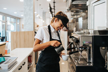 Beautiful And Happy Young Female Worker Working In A Bakery Or Fast Food Restaurant And Using Coffee Machine. Positive People In Small Business Concept.