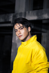 an Asian man with sleek black hair wearing a yellow jacket and jeans while posing