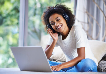 Sticker - Social media at her fingertips. a young woman sitting at home using a laptop and wearing headphones.