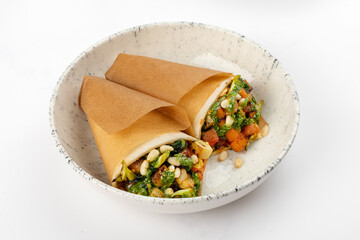 2 vegetarian rolls with carrots, broccoli, tofu, tomatoes, zucchini, pine nuts and pesto sauce on a round white plate on a white background. Close up 3/4