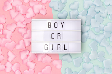 Boy or girl. Lightbox with letters and confetti in a heart shape on a pink and blue background. Gender reveal concept.