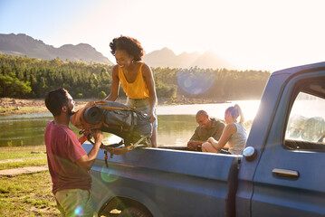 Group Of Friends Unloading Backpack From Pick Up Truck On Road Trip By Lake In Countryside