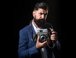 © Volodymyr - Young man using a professional old camera. Portrait of serious man photographer with vintage retro old film camera isolated on a black background.