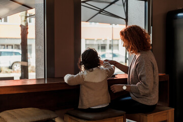 Beautiful young red-haired mother with cute curly-haired daughter are sitting in cozy cafe and drinking hot school. Mothers Day. Warm.