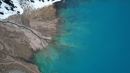 Wall Mural - A lake in the mountains with turquoise blue water. Drone view of clear water, coniferous trees and snowy mountains. People walk along the shore, low bushes grow. Big Almaty lake. Kazakhstan