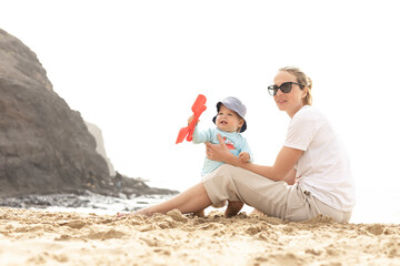 Wall Mural - Mother playing his infant baby boy son on sandy beach enjoying summer vacationson on Lanzarote island, Spain. Family travel and vacations concept