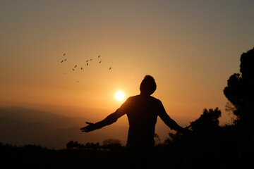 Man with open arms at sunset conveying a sense of freedom.
