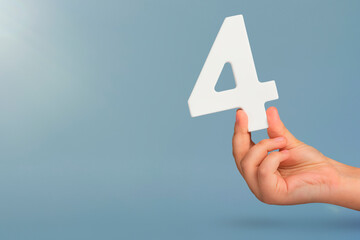 Fototapete - number four in hand. Hand holding white number 4 on blue background with copy space. Concept with number four. Birthday 4 years, fourth grade, four day work week