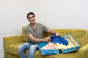 Young man sits on sofa and packs a suitcase for vacation