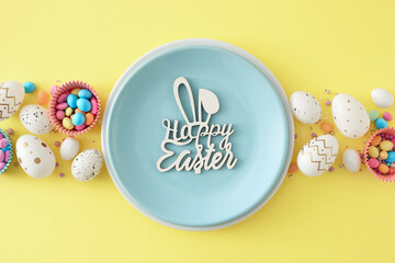 Wall Mural - Easter concept. Flat lay photo of blue plate with inscription happy easter bunny ears colorful eggs dragees in baking molds sprinkles on pastel yellow background