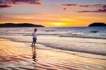 Wall Mural - Child playing on ocean beach. Kid at sunset sea.