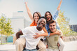 © Jose Calsina - Two multiracial young friends giving piggybacks ride to his girlfriends. A group of happy people having fun and smiling at weekend activity. Men carrying women on his shoulders looking at camera. High