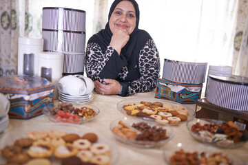 Wall Mural - Something for everyone. a mature muslim woman sitting in front of a variety of sweet cakes.