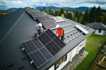 engineers building photovoltaic solar module station on roof of house. men electricians in helmets i