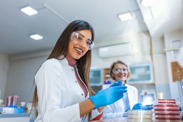 microbiologist hand cultivating a petri dish whit inoculation loops, beside a microscope and at background tubes and tools of laboratory, lab technician hand planting a petri dish