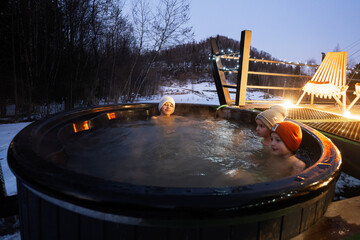 Wall Mural - Kids enjoying bathing in wooden barrel hot tub in the terrace of the cottage. Scandinavian bathtub with a fireplace to burn wood and heat water.