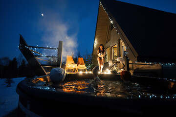 Wall Mural - Kids enjoying bathing in wooden barrel hot tub in the terrace of the cottage. Scandinavian bathtub with a fireplace to burn wood and heat water.