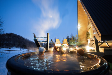 Wall Mural - Family enjoying bathing in wooden barrel hot tub in the terrace of the cottage. Scandinavian bathtub with a fireplace to burn wood and heat water.