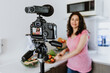 © Marcos - Latin woman influencer recording video class or live stream with camera about healthy eating and nutrition in kitchen at home in Mexico, hispanic people
