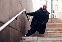 Hypebeast culture - young African American man with attitude walking down public city stairs - streetwear hip hop fashion - person dressed in black with a red beanie