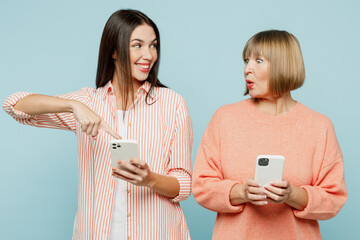 Wall Mural - Shocked amazed elder parent mom with young adult daughter two women together wear casual clothes hold use point finger on mobile cell phone isolated on plain blue cyan background. Family day concept.