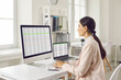 © Studio Romantic - Side view portrait of a concentrated young business woman accountant sitting at the desk and working on a laptop with tables and charts at office or at home and looking to the monitor screen.