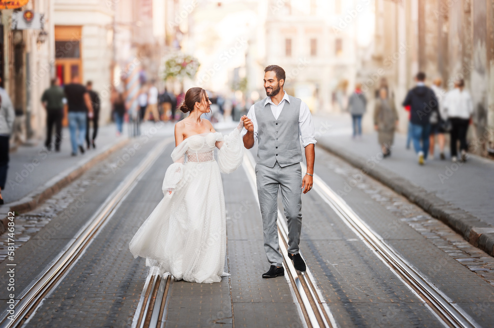 Young happy wedding couple walking holding hands through the old ...