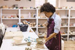 © mitarart - Creativ African American woman proudly stands in her pottery studio, skillfully decorate a clay cup with her hands. Her creative work is the result of years of practice as an artisan potter.