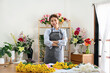 © Katcha - Female florist in apron smiling and standing with arms crossed i