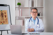 © Katcha - Confident senior male doctor with stethoscope to working on lapt
