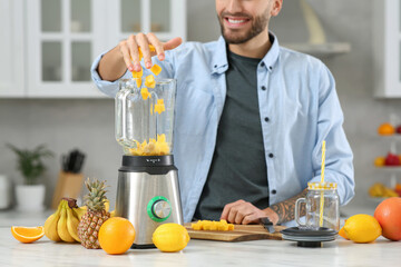 Canvas Print - Man adding mango into blender with ingredients for smoothie in kitchen, closeup