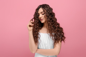 beautiful young woman with long curly brown hair on pink background