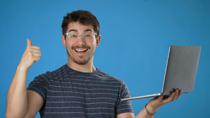 Wall Mural - Young smiling happy man 20s in striped t-shirt hold use work on laptop pc computer browsing chatting surfing internet isolated on plain blue background studio portrait. People lifestyle concept