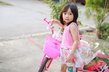 Wall Mural - Portrait image of 5-6 years old kid. Happy Asian child girl ride a bike at the park outdoor. Exercise for health and sport. Summer season.