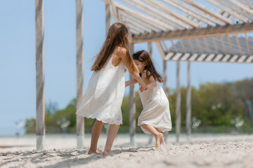 two happy little girls with long hair in summer dresses play on a sandy beach in summer