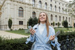 © LIGHTFIELD STUDIOS - happy young woman in blue trench coat holding laptop and smartphone near historical building in Vienna.