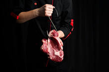 Raw Steak On A Meat Hook In The Hands Of A Chef. Meat. On A Black Background.