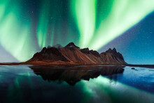 Aurora Borealis Northern Lights Over Famous Stokksnes Mountains On Vestrahorn Cape. Reflection In The Clear Water On The Epic Skies Background, Iceland. Landscape Photography