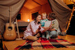 © bondvit - Happy family with lovely baby playing and read book together in glamping on summer evening. Luxury camping tent for outdoor recreation and recreation. Lifestyle concept