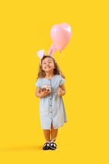 Poster - Little girl in bunny ears with Easter cake and balloon on yellow background