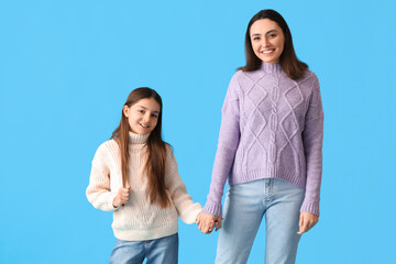 Wall Mural - Little girl and her mother in knitted sweaters holding hands on blue background