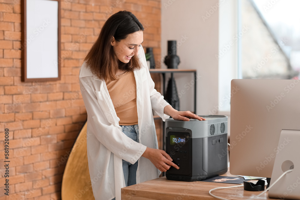 Young woman with portable power station at table in office