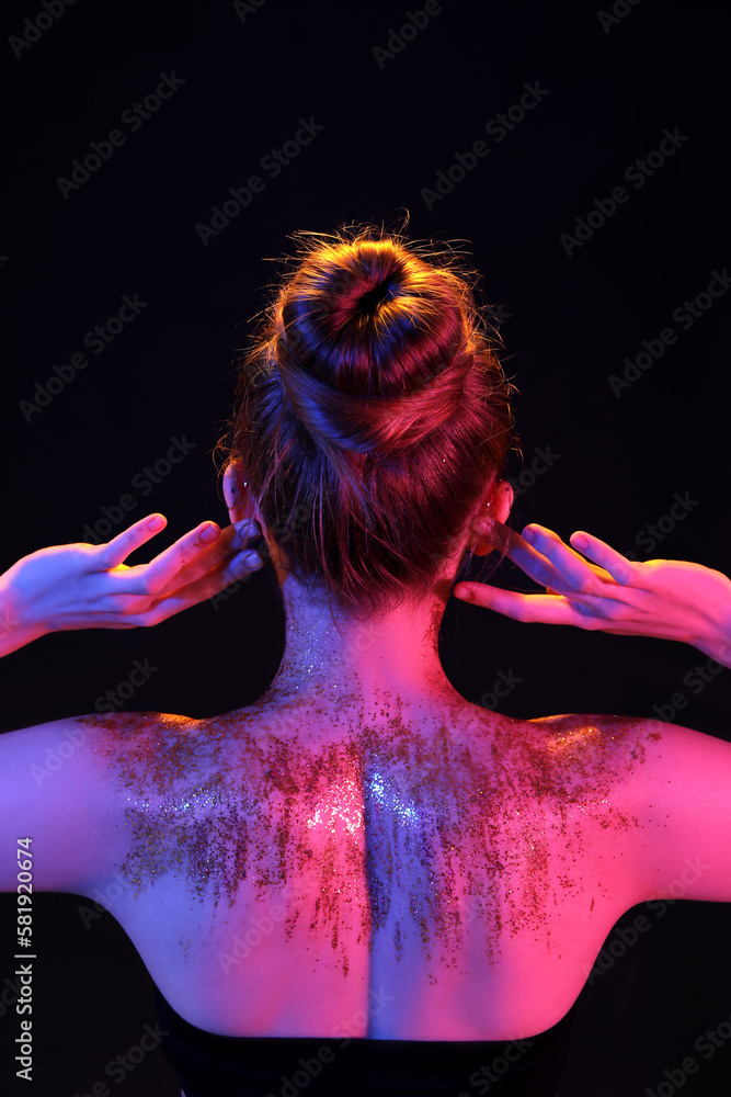 Young woman with glitter on her body on dark background, back view