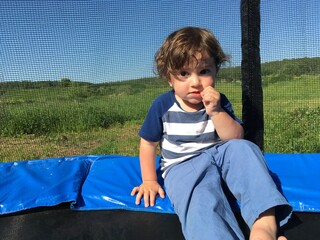 surprised looking curly child boy sucking thumb sitting on a trampoline