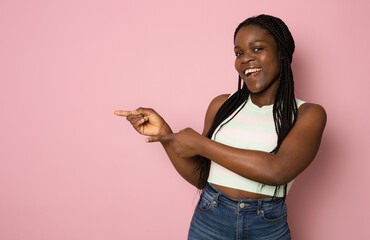 Young african american woman wearing white t-shirt standing over isolated pink background smiling and looking at the camera pointing with two hands and fingers to the side.