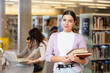 © JackF - Successful young female student standing with books near bookshelves in library. Concept of self-education and knowledge ..
