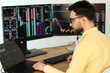 © Maria Vitkovska - Serious handsome man trader using laptop computer working online with crypto chart sitting in modern office. Broker research stock market. Successful business, online trading concept