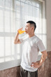 © Anciens - Asian man is drinking juice near the window in the morning.