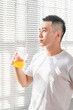 © Anciens - Asian man is drinking juice near the window in the morning.